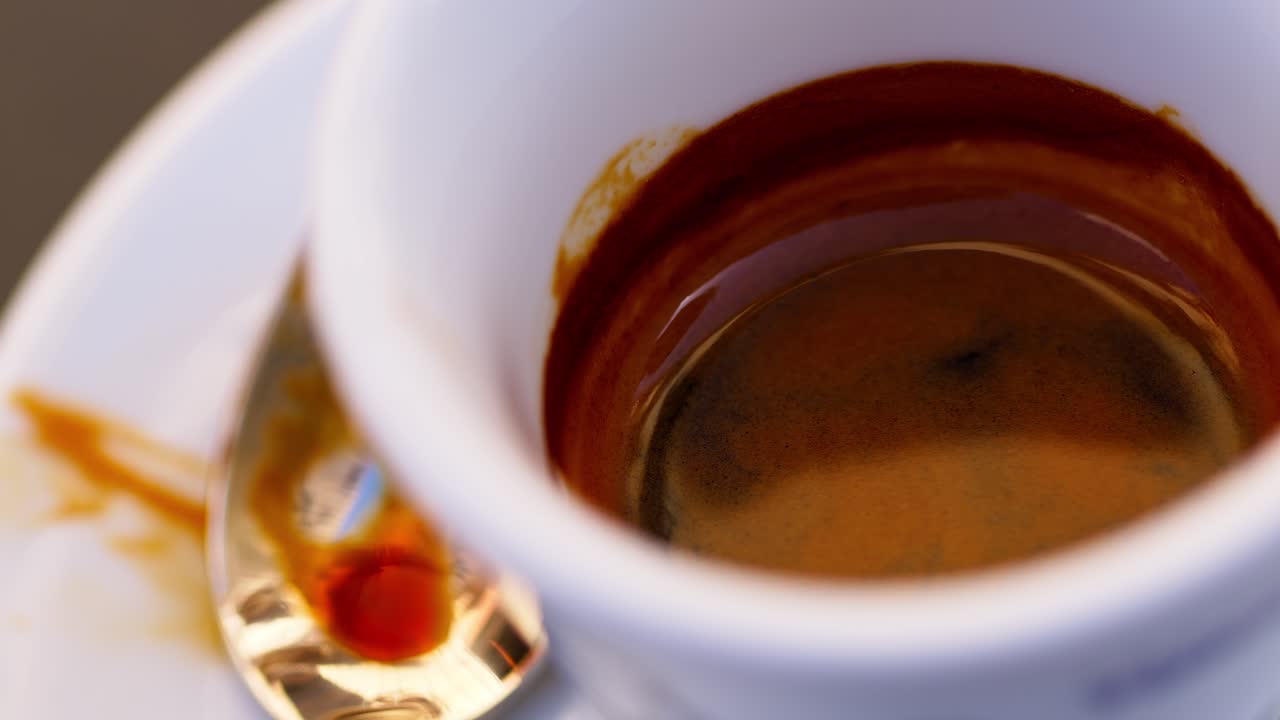 Macro panning shot of espresso cup with a spoon beside it in a cozy cafe setting
