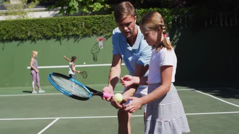 caucasian father teaching his daughter to play tennis at tennis court on a bright sunny day