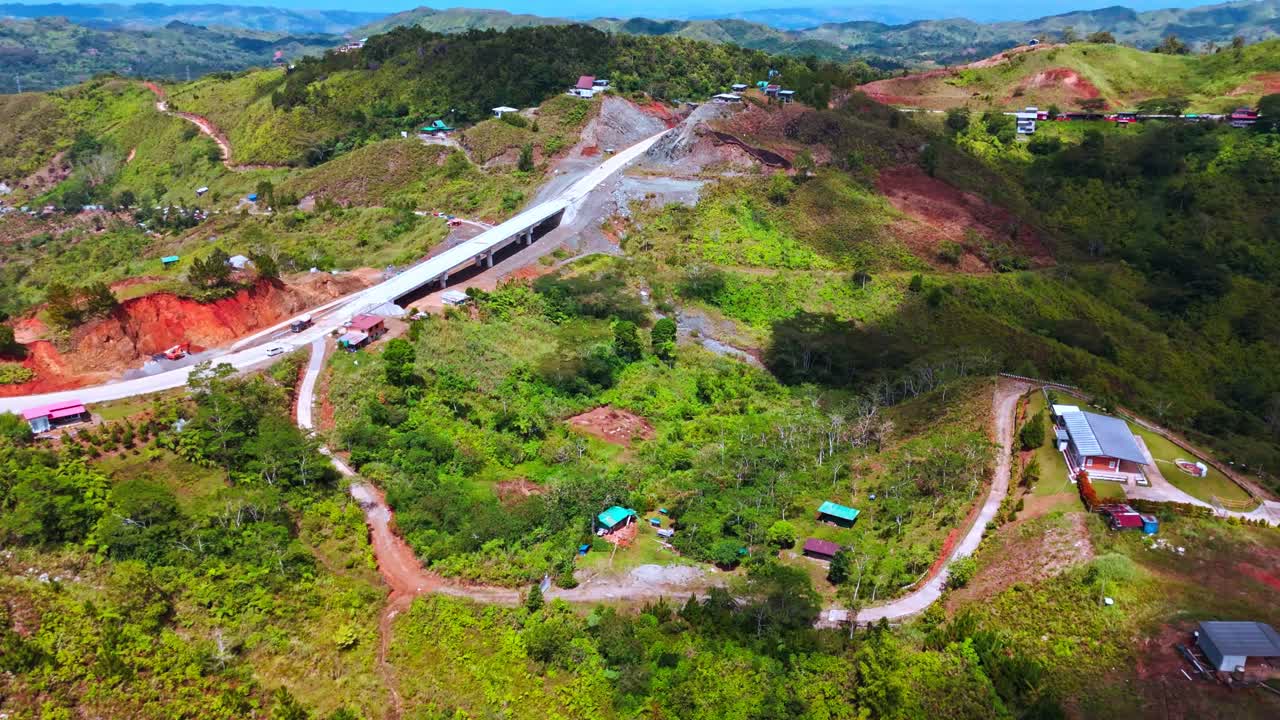 Drone view of a modern concrete bridge construction cutting through the lush green mountains of Davao. Rural infrastructure development connecting remote highland areas in the Mindanao region
