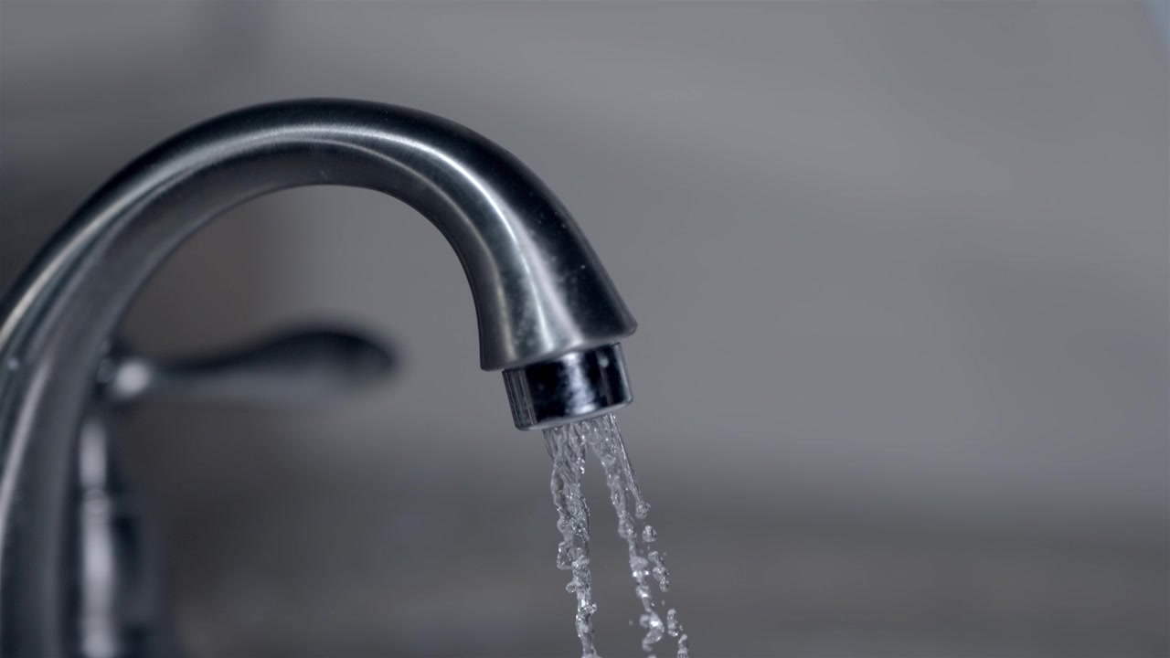 Close up of a hand turning on the faucet with water starting to flow