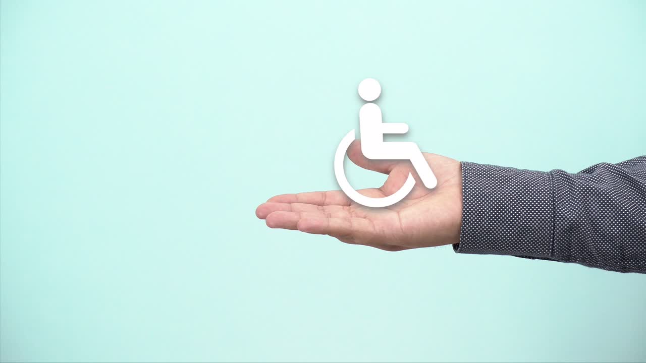 concept of disability. hand shows symbol of person in wheelchair on blue background.