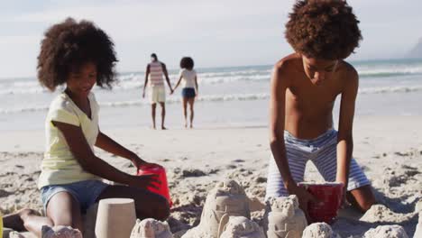 hermano y hermana afroamericanos jugando con arena en la playa