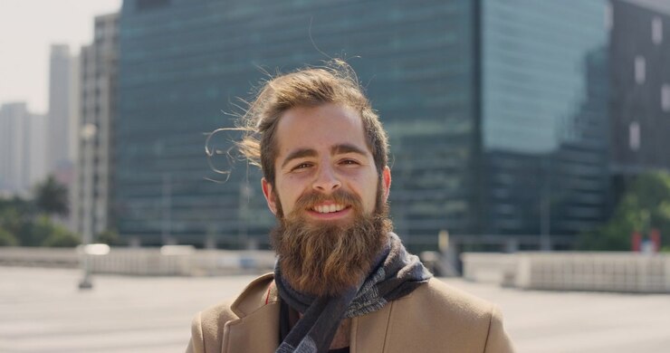 Portrett av en smilende ung mann med skjegg i et urbant miljø
