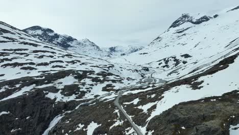 Top-of-Trollstigen-Trolls-road-in-Norway-during-spring---Aerial-of-road-leading-into-vast-mountain-valley-during-springtime-with-still-snow-left-in-the-terrain