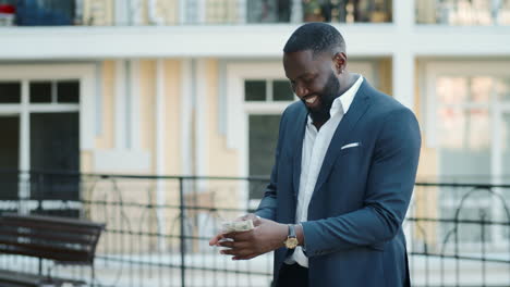 cheerful businessman smelling dollars at urban street. afro guy holding cash