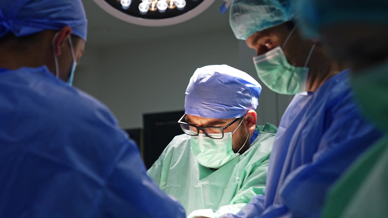 Chirurgo maschio barbuto che utilizza strumenti durante un'operazione. L'équipe medica esegue un intervento chirurgico per trauma.