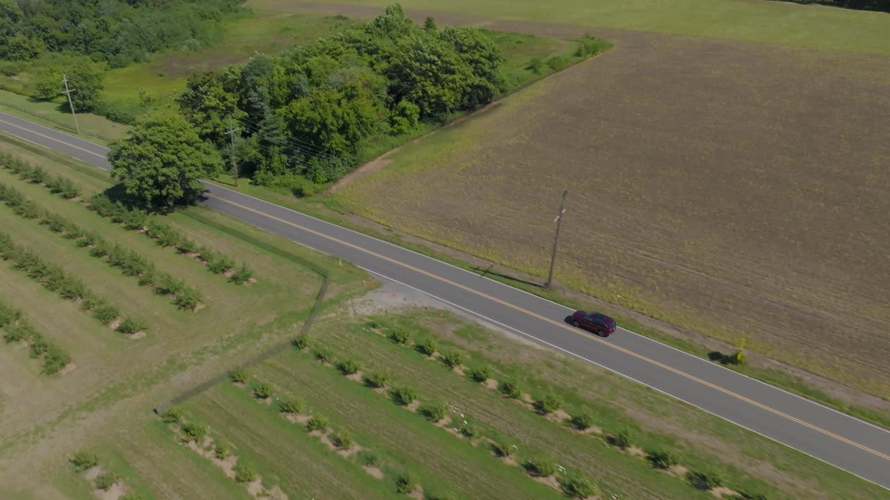 A drone follows a red car driving along a scenic country road
