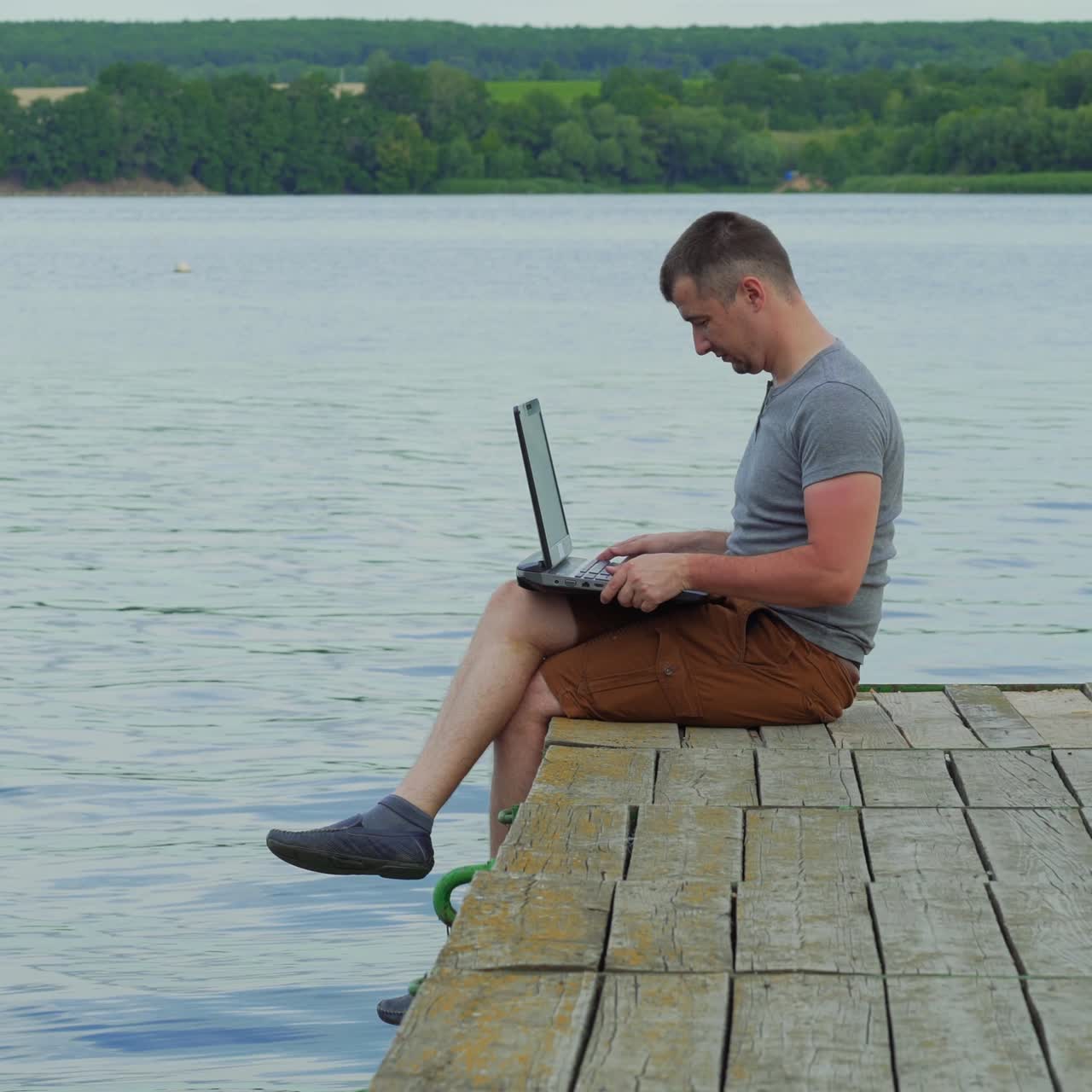 Young man working on laptop while sitting ?n old pier