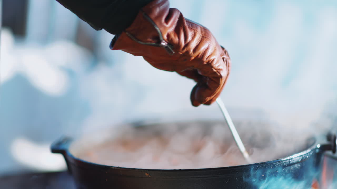 Gloved hand stirring steaming bowl of moose soup in Swedish outdoor winter cooking