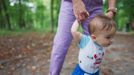baby spending time outdoors in the green summer park. little toddler walks by the path held by his mom. close up.