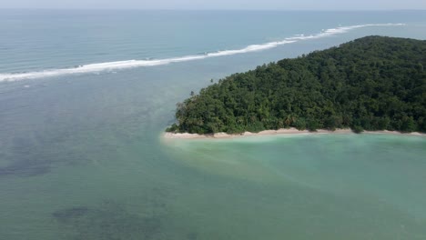 drone rotates around green island surrounded by clear ocean water