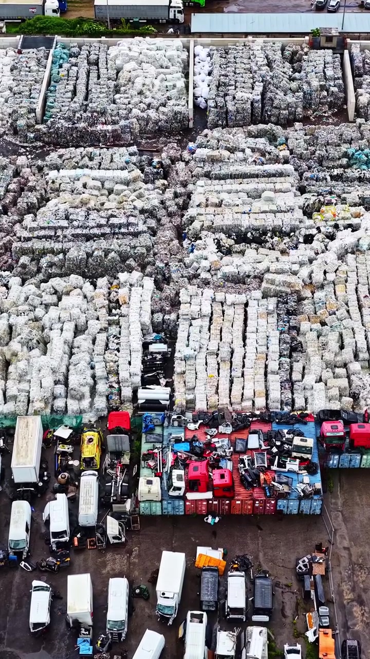Luftaufnahme einer Recyclinganlage mit Lastwagen und Ballen aus gepresstem Plastikmüll.