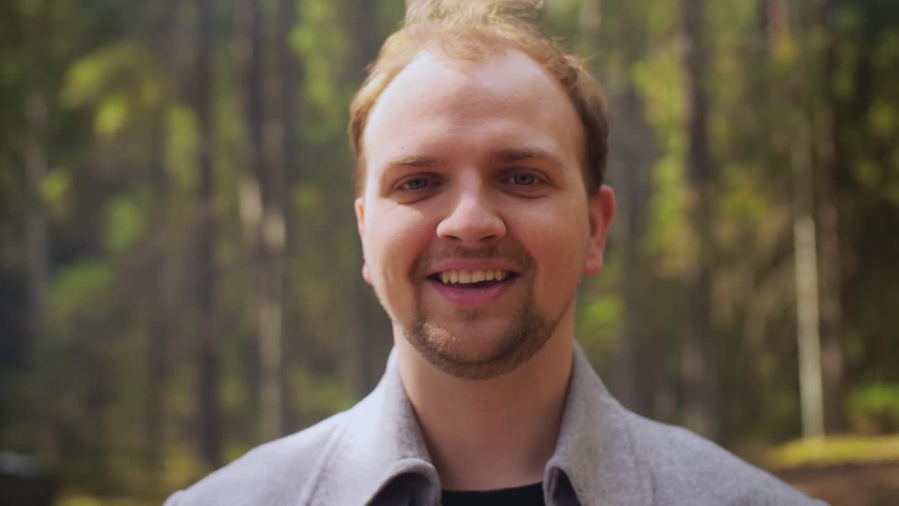 Close-up portrait of young handsome man standing outdoors in the forest or park smiling looking at camera.