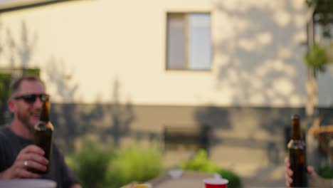 Close-up-a-group-of-young-friends-clink-glasses-together-at-a-table-during-lunch-in-the-courtyard-of-a-suburban-house