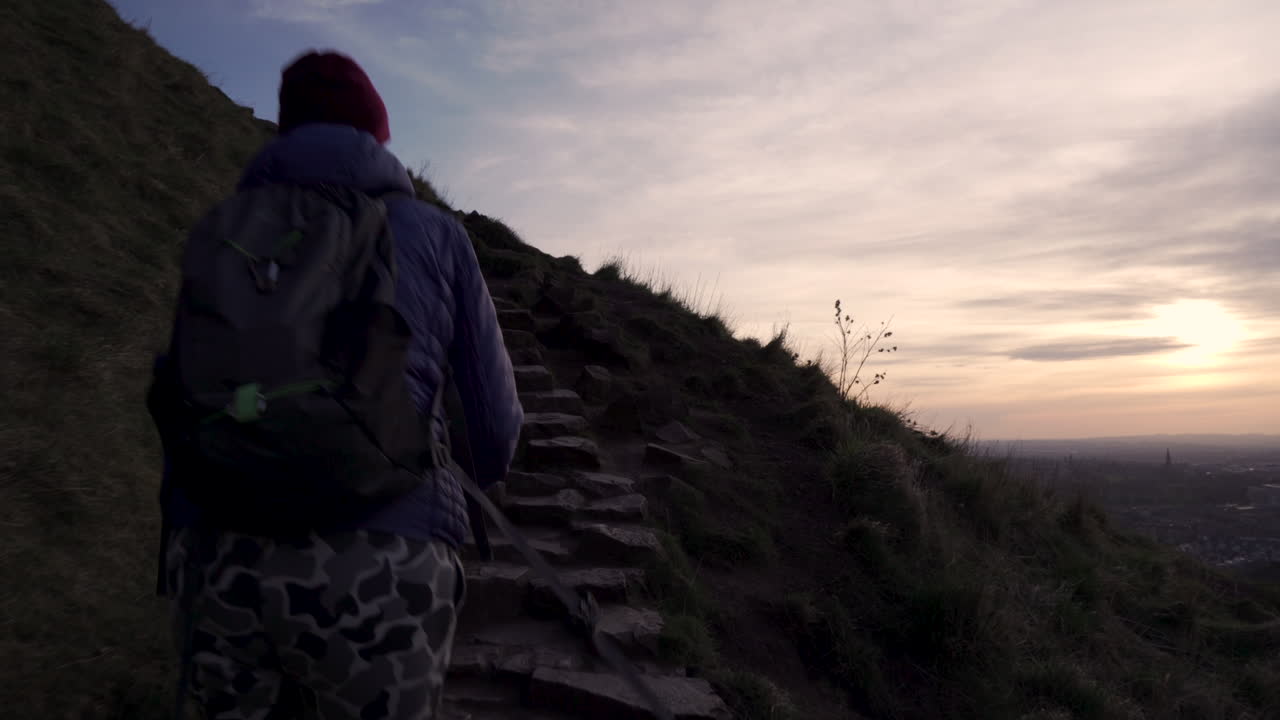 primer plano de una chica caminando por la montaña arthurs seat en la ruta de senderismo por la noche durante la hora dorada con la ciudad de edimburgo en el fondo abajo