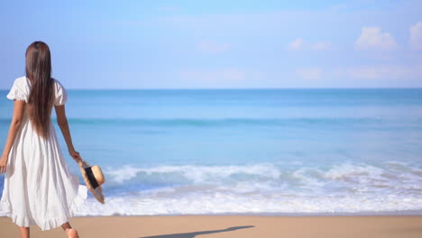 happy asian woman in white sundress walking on the white sand beach at seafront raising her hands up turning around enjoying freedom at a tropical island