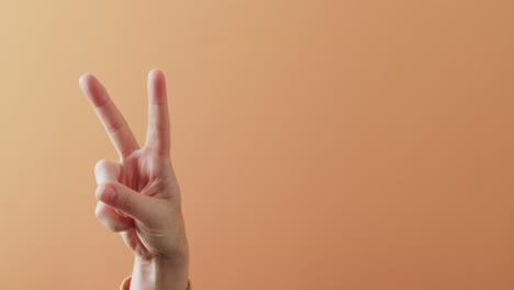 cerca de la mano de la mujer cacausiana mostrando el signo de la paz con espacio de copia en fondo naranja.