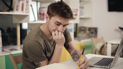 young attractive programmer thinking hard about something while sitting beside his laptopin a classroom.