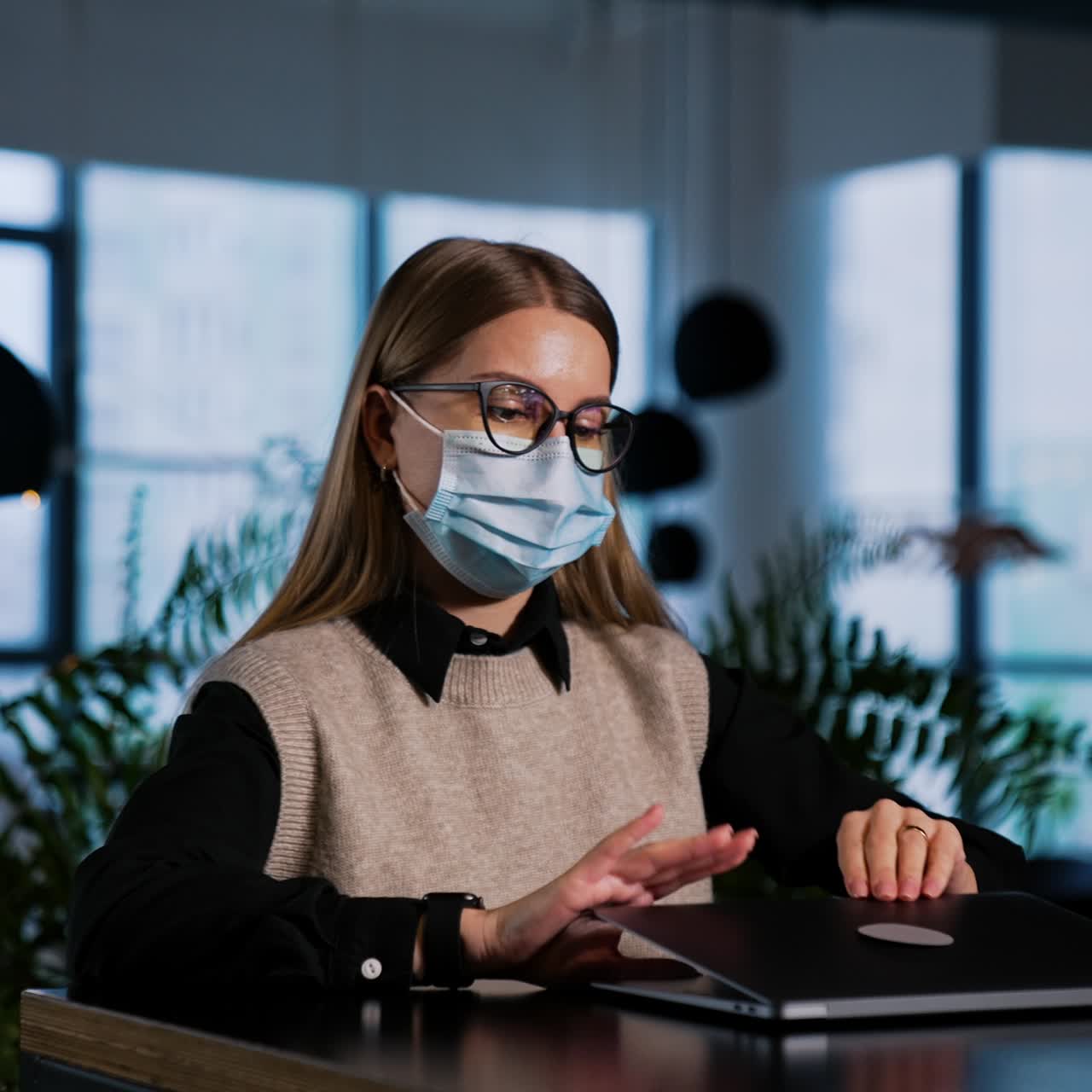 Focused lady in mask works at her laptop in office. Businesswoman closes laptop, puts off her glasses and mask putting them on computer