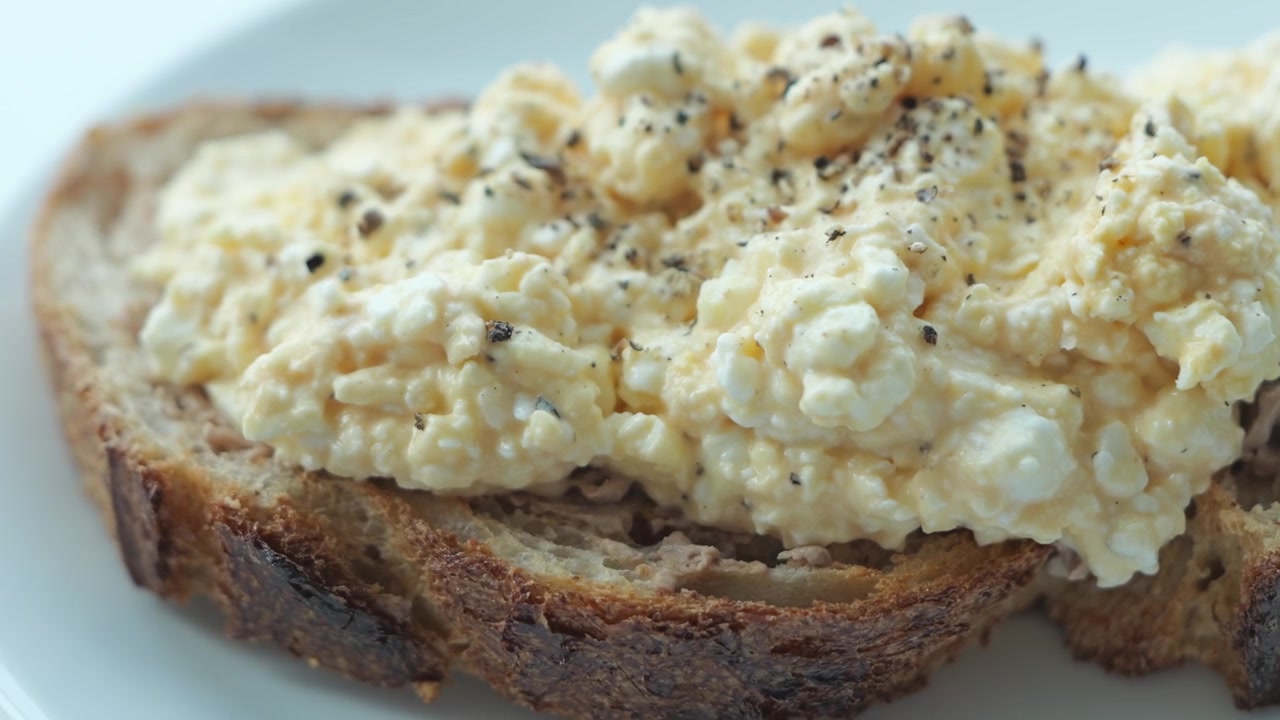 Primo piano di pane tostato guarnito con uova sode schiacciate, fiocchi di latte e salsa maionese cremosa, che crea una colazione fatta in casa ricca e appetitosa