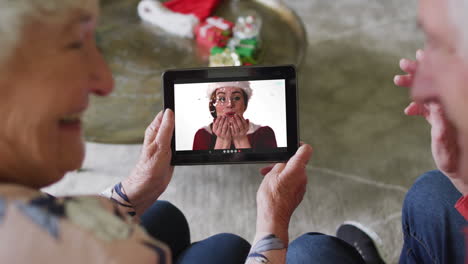 pareja caucásica mayor usando una tableta para una videollamada de navidad con una mujer feliz en la pantalla
