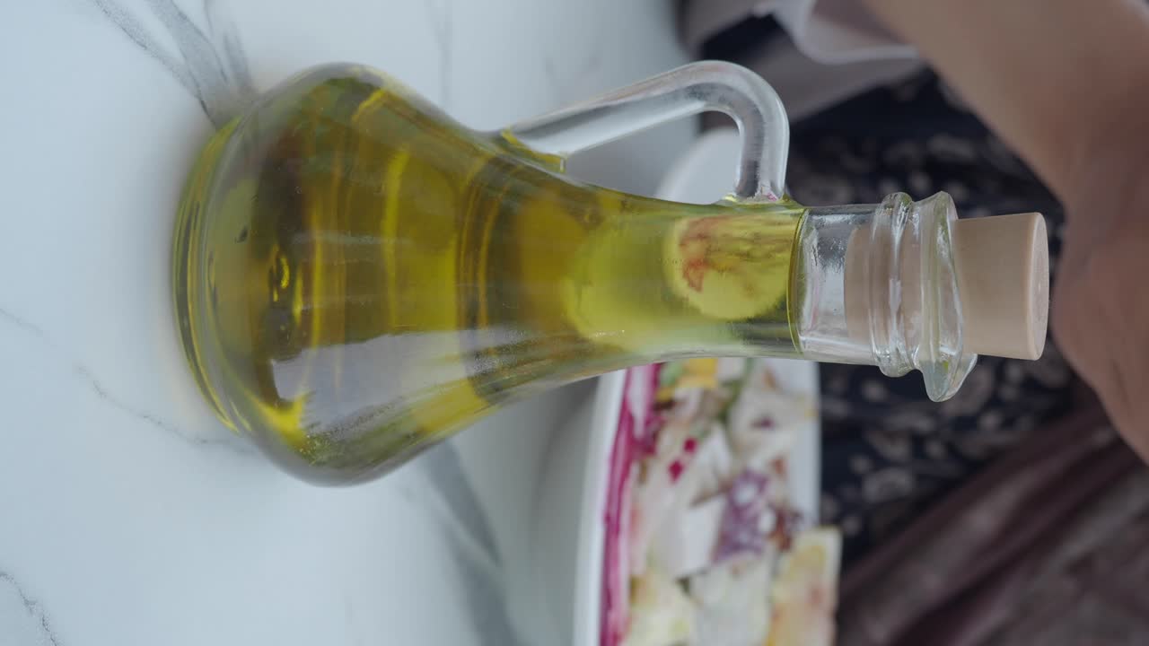 Close-up of an olive oil bottle on a marble table with a person eating salad