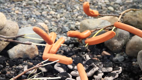 hot dogs cooking on sticks over campfire