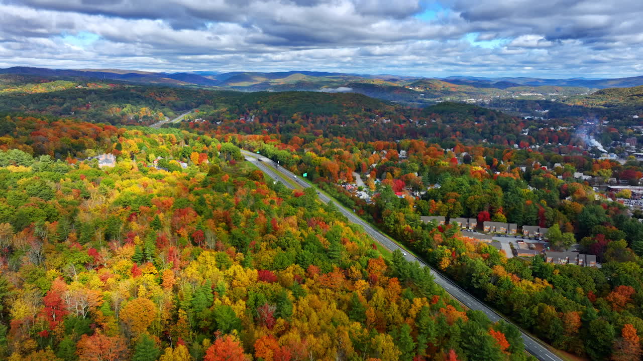Colorful autumn forests cover the mountainous landscape. Highways cross the beautiful scenery. Overcast sky above the view.