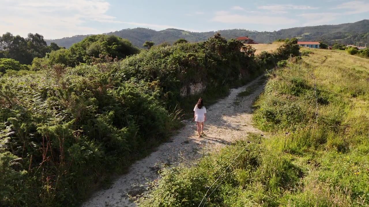 Mulher com liberação de modelo caminhando em um caminho rural ensolarado entre sebes verdes.