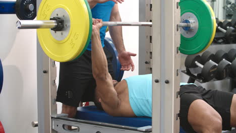 Trainer-assisting-man-bench-pressing-barbells-at-a-gym