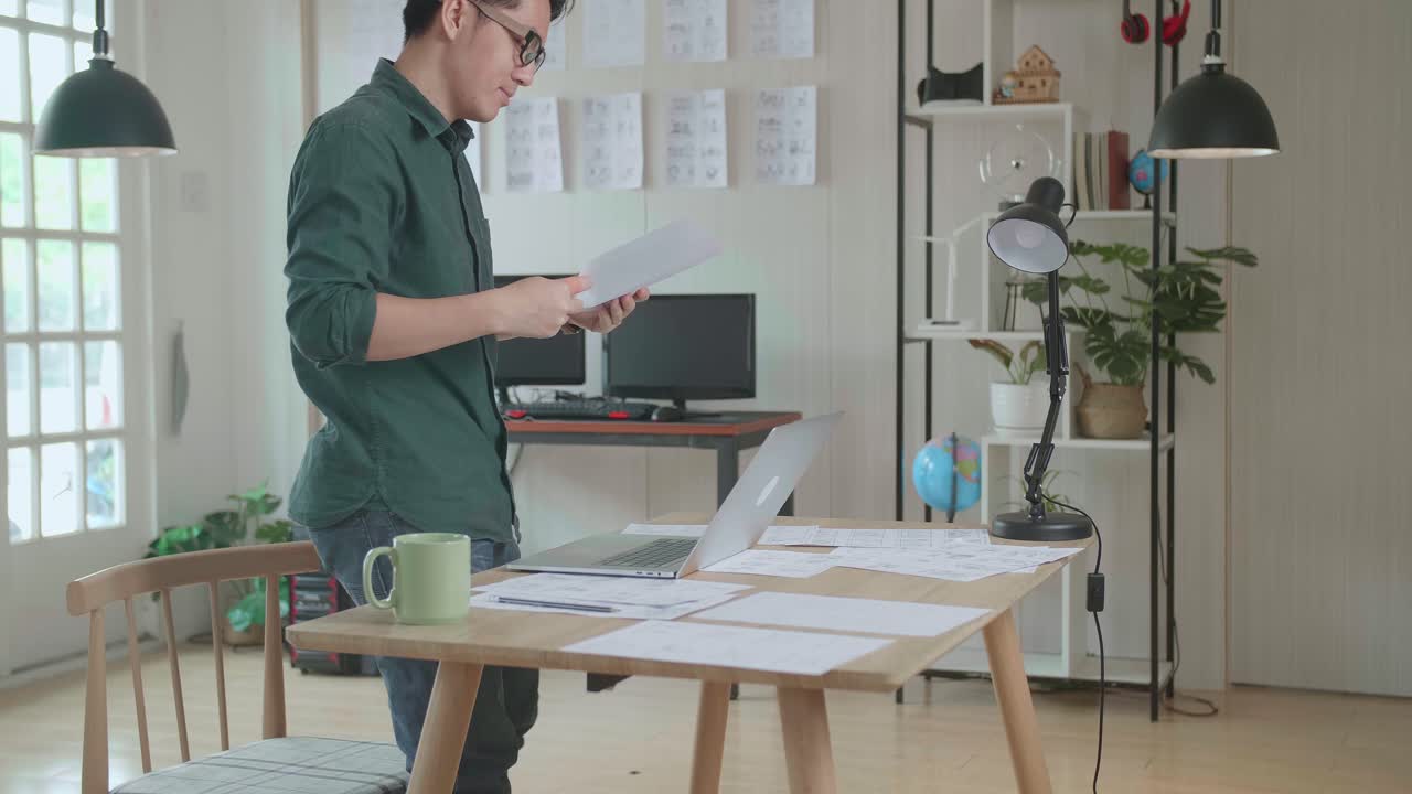 Creative Asian Designer Works On A Storyboard, Looks At His Sketches And Concepts, Choosing The Best Drawings For His Project. Video Editing, Comics Compilation, Application Ui Or Game Plot