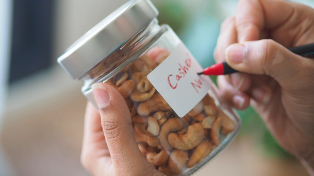 Close-up of Hand Labeling a Jar of Cashew Nuts