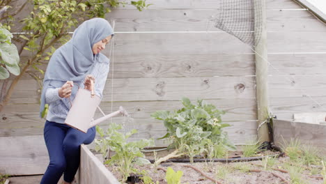 Glückliche-Biracial-Frau-In-Hijab,-Die-Pflanzen-Gießt,-Gartenarbeit-Mit-Kopierraum,-Zeitlupe