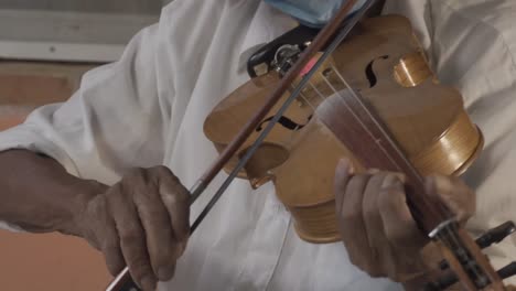 captura de pantalla de un músico de edad hispana con un sombrero y una máscara tocando el violín en la calle