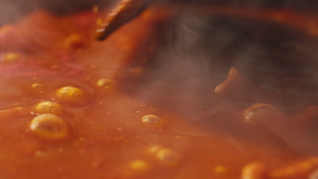 Chicken in tomato sauce is boiling on a frying pan with spices. Cooking tomato sauce curry with chicken fillet. Traditional Italian Mexican Asian dish. High quality studio shot for cafe, restaurant close up.