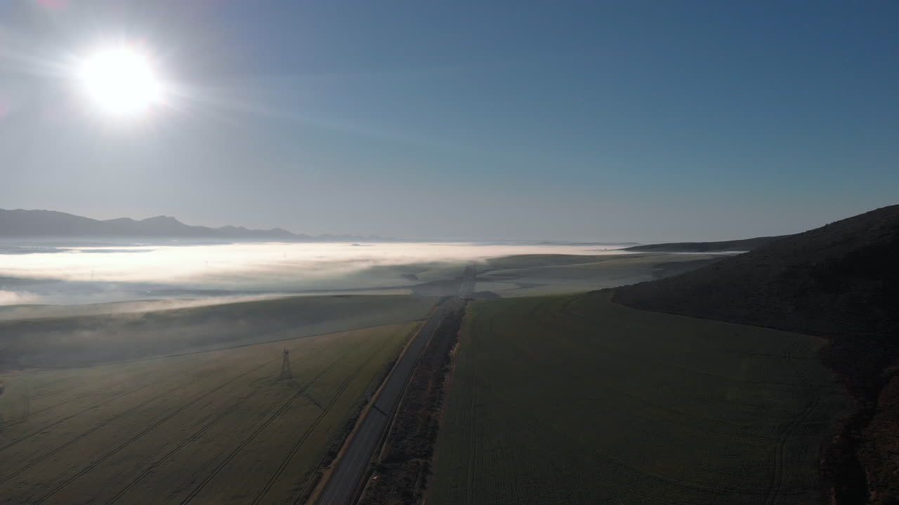 안개가 자욱한 평야의 넓은 공중 전망과 산을 배경으로 아침 시간에 황량한 도로