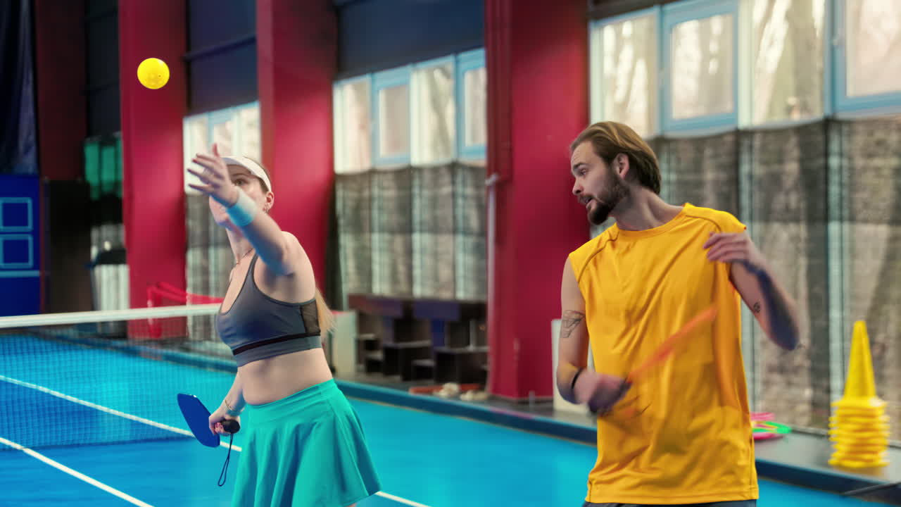 A man teaching a woman how to play pickleball in an inside court