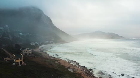 drone captures serene sea waves gently reaching base of majestic foggy mountains. the misty weather adds mystical ambiance to scene in iceland