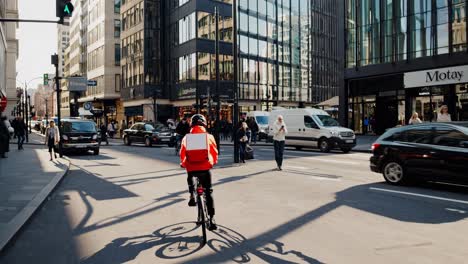 bike messenger carrying thermal backpack weaving through bustling downtown street, skillfully navigating heavy traffic and pedestrian filled urban landscape during daylight hours