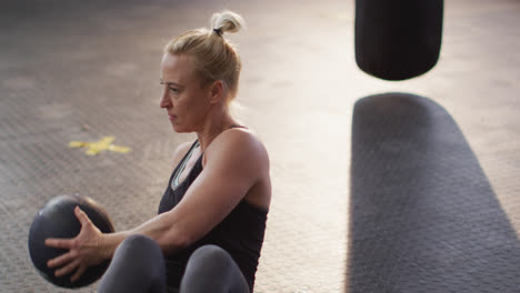 Fit-caucasian-woman-performing-abs-exercise-with-medicine-ball-at-the-gym