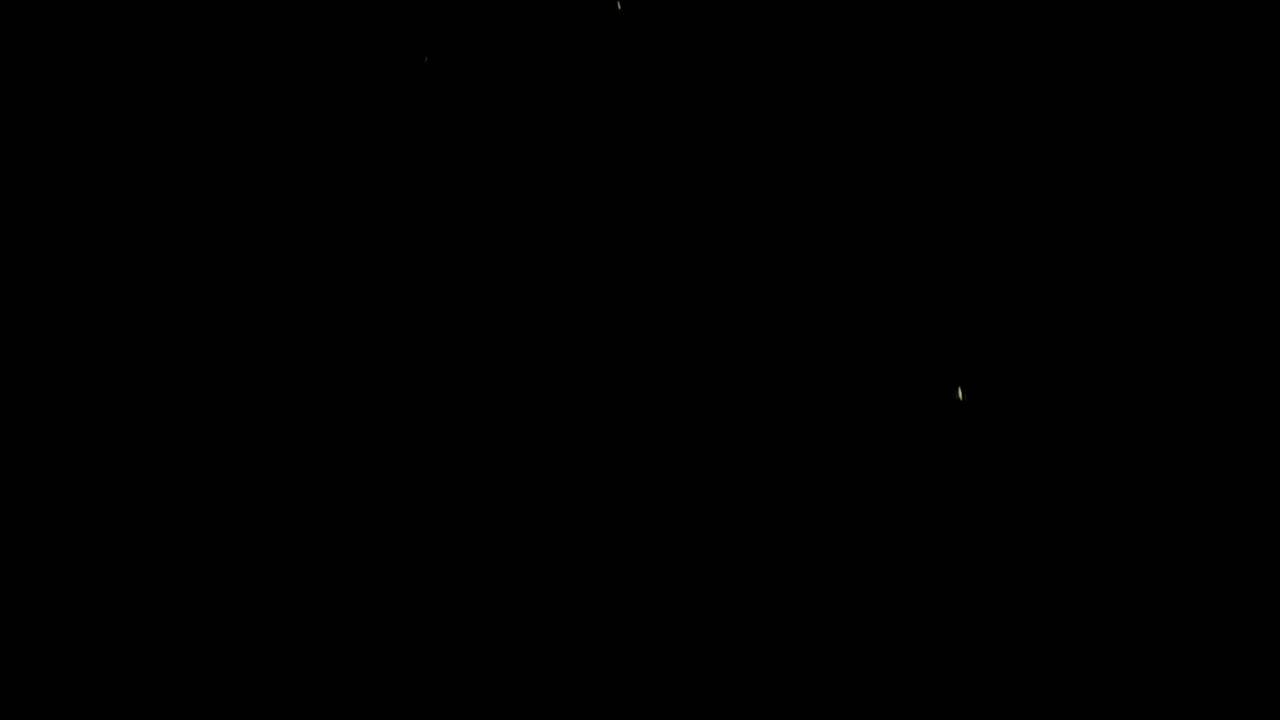 Slow motion wide shot of fine gold flakes falling and flickering in sparse formation on black background.