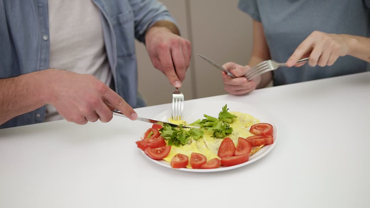Young family couple enjoying breakfast time together eating omelette from single plate, daily routine girlfriend love caring relationship sitting at bar table together. Man feeding his beloved