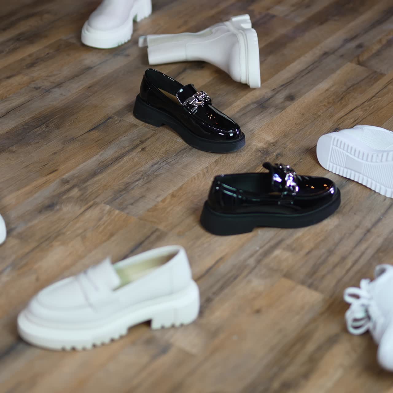 Woman in massive black shoes walks among the scattered footwear. Lady picks up another pair of black shoes leaving white ones on the floor