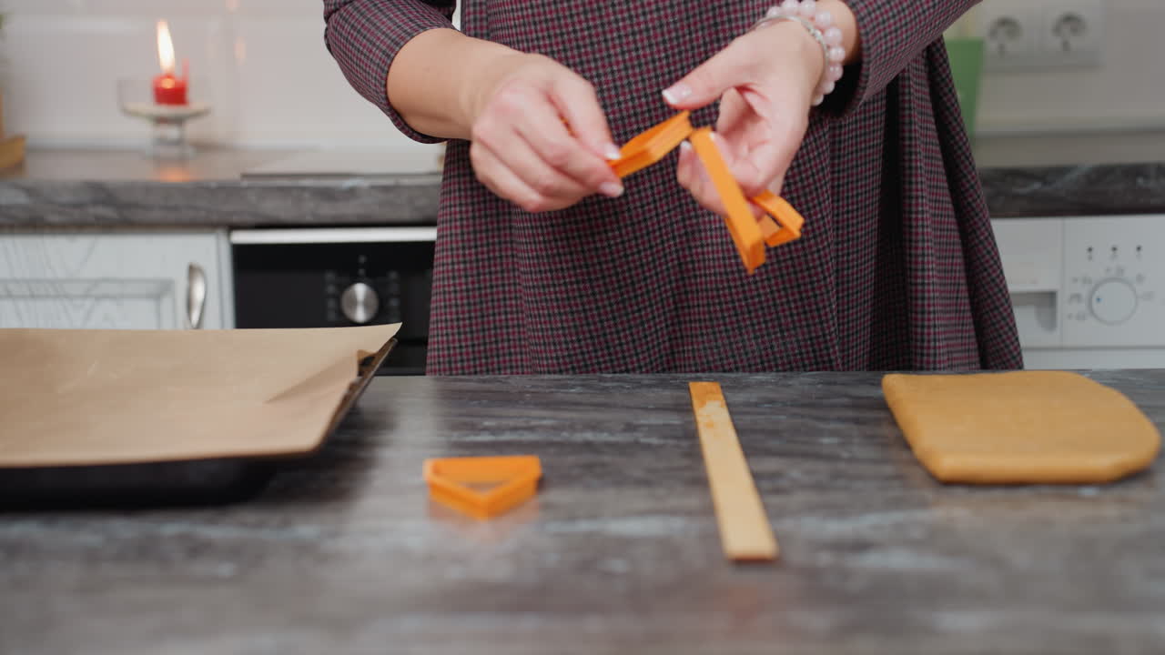 panadero en vestido a cuadros arregla formas de horneado naranja en la encimera en la cocina moderna, preparándose para hacer pasteles con iluminación cálida, backsplash de azulejos y vela roja en el fondo
