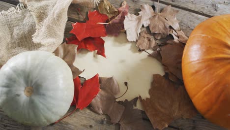 paper with copy space against autumn leaves and pumpkins on wooden surface