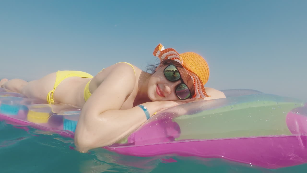 Attractive Woman In An Orange Hat Floats In The Sea On An Inflatable Mattress