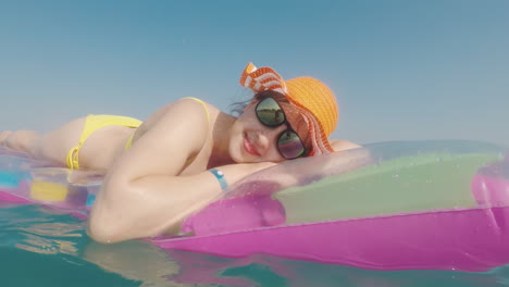 attractive woman in an orange hat floats in the sea on an inflatable mattress