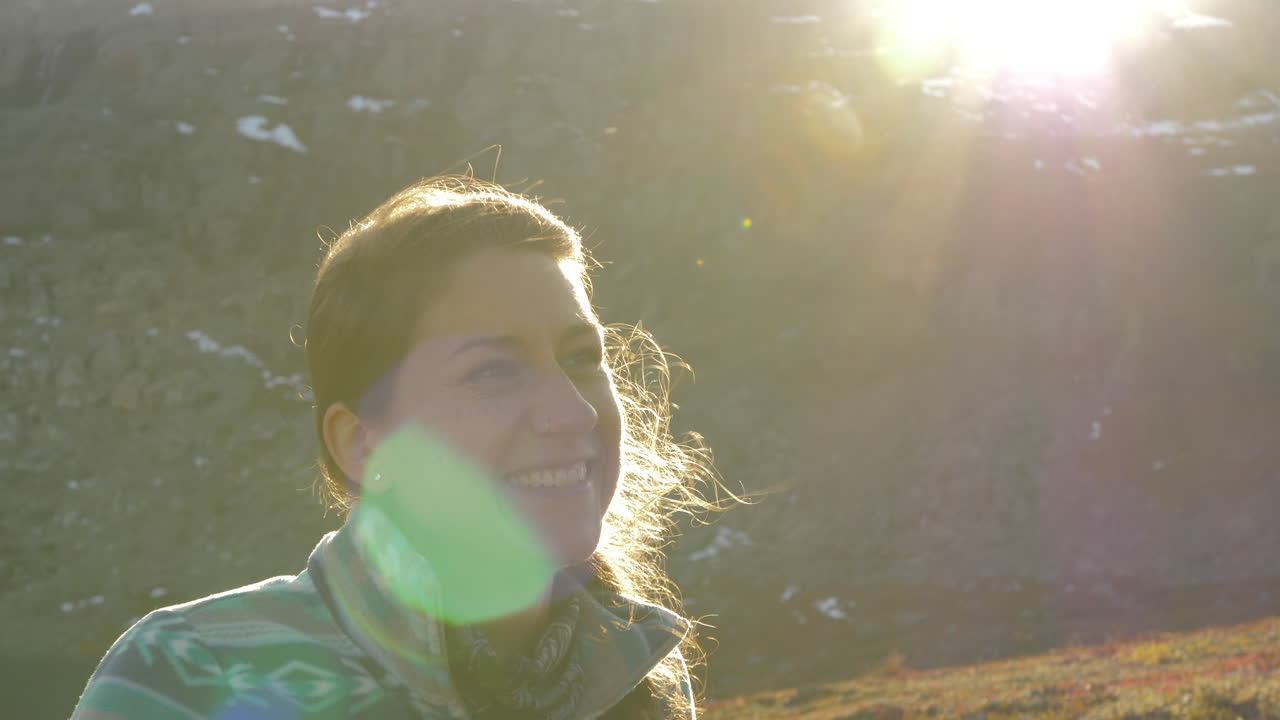 cerca de una mujer sonriendo y riéndose durante una caminata al atardecer en una montaña en noruega, cámara lenta con destellos de lente