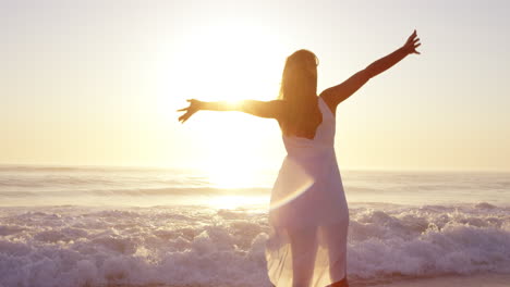 free happy woman with arms outstretched enjoying nature walking along beach at sunset face raised towards sky