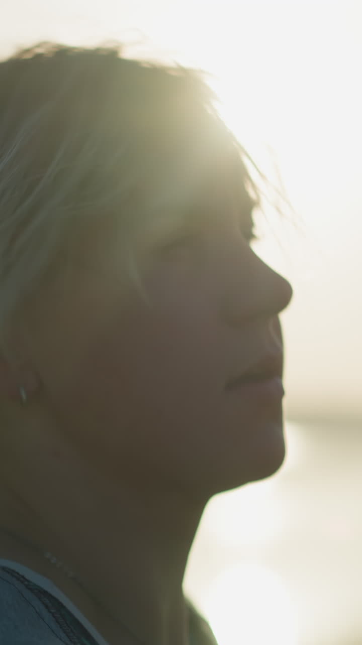 una mujer joven comienza a quitarse el casco con una mano mientras se cepilla suavemente el cabello hacia atrás con la otra, mientras la luz del sol se refleja en ella